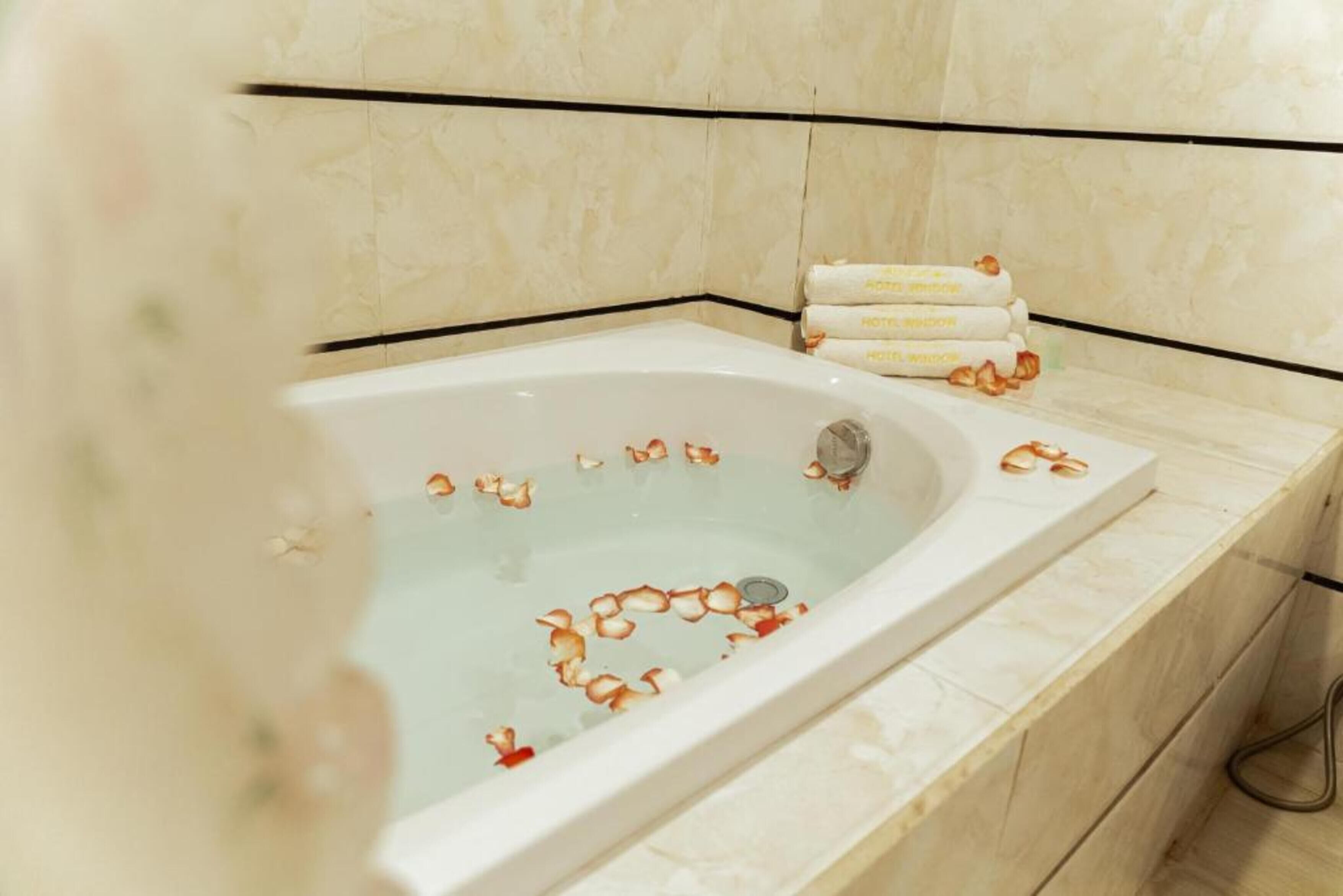 A bathtub with rose petals and a set of towels on the side.