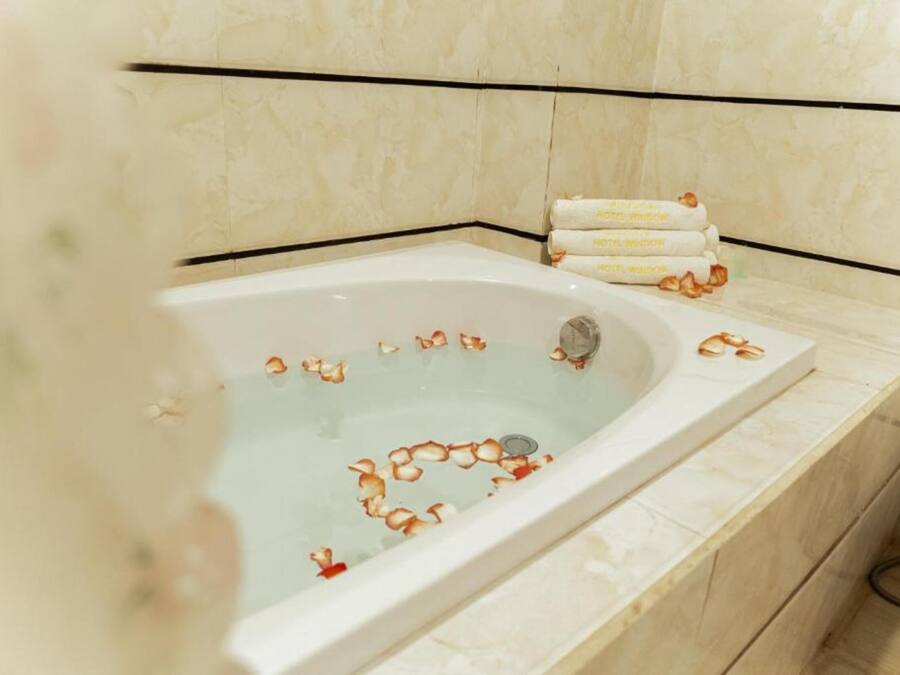 A bathtub with rose petals and a set of towels on the side.