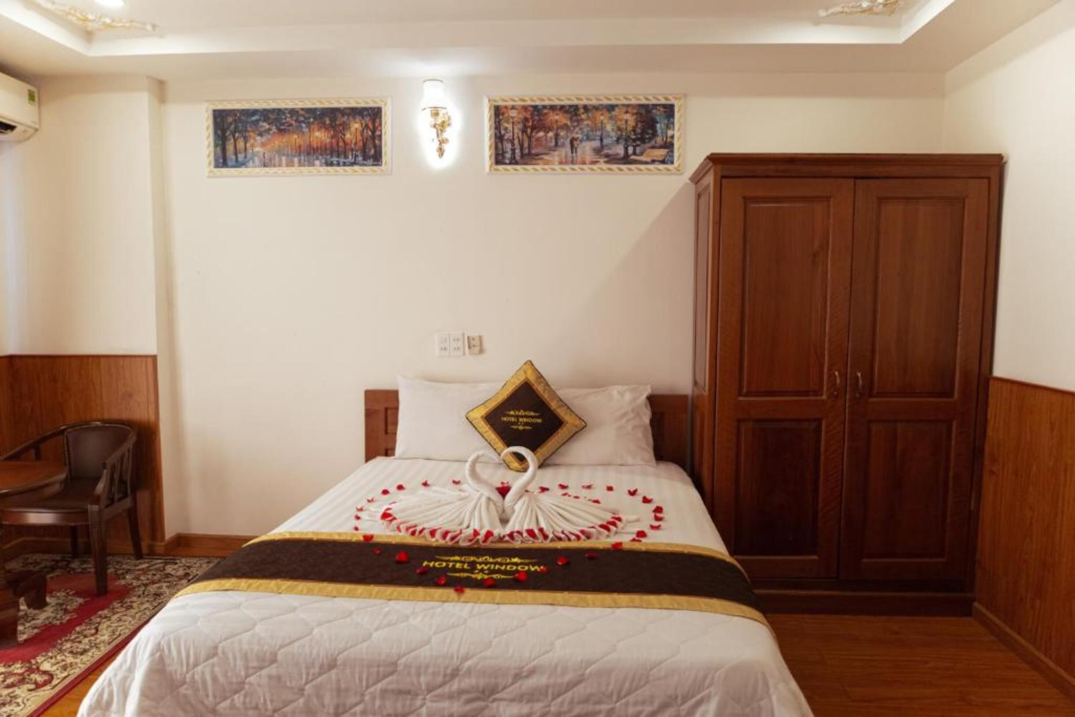 A hotel room with a bed, a wooden wardrobe, a desk, and two paintings on the wall.