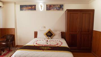 A hotel room with a bed, a wooden wardrobe, a desk, and two paintings on the wall.