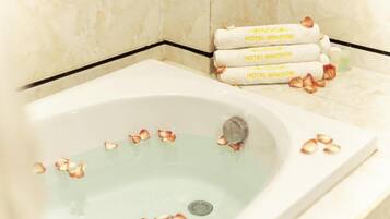 Eine Wanne mit darin treibenden Rosenblüten, ein Handtuchhalter mit Handtüchern, auf denen "HOTEL WINDOW" steht, und eine Wand mit Marmorfliesen.