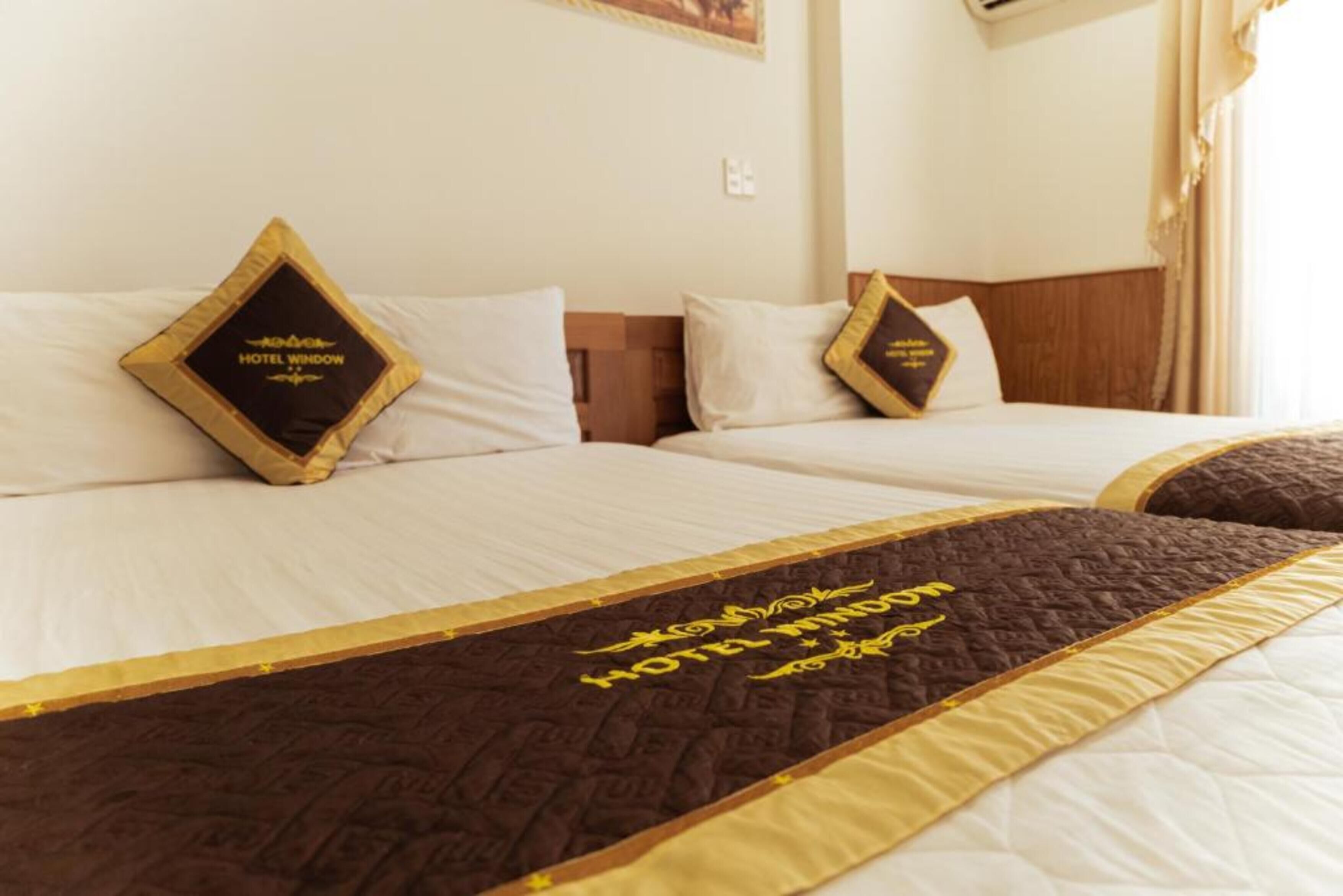 A hotel room with two beds, each with a pillow that has the hotel's name. There is a decorative quilt on the bed between the beds.