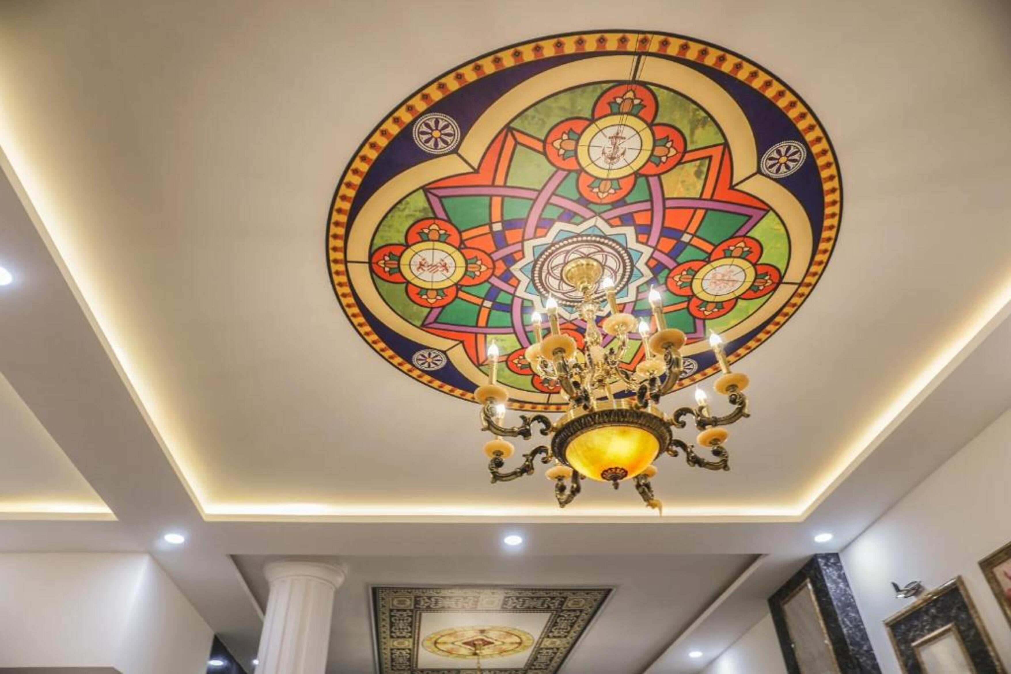 A chandelier with multiple lights hanging from the ceiling, a decorative ceiling design, and a framed artwork on the wall.