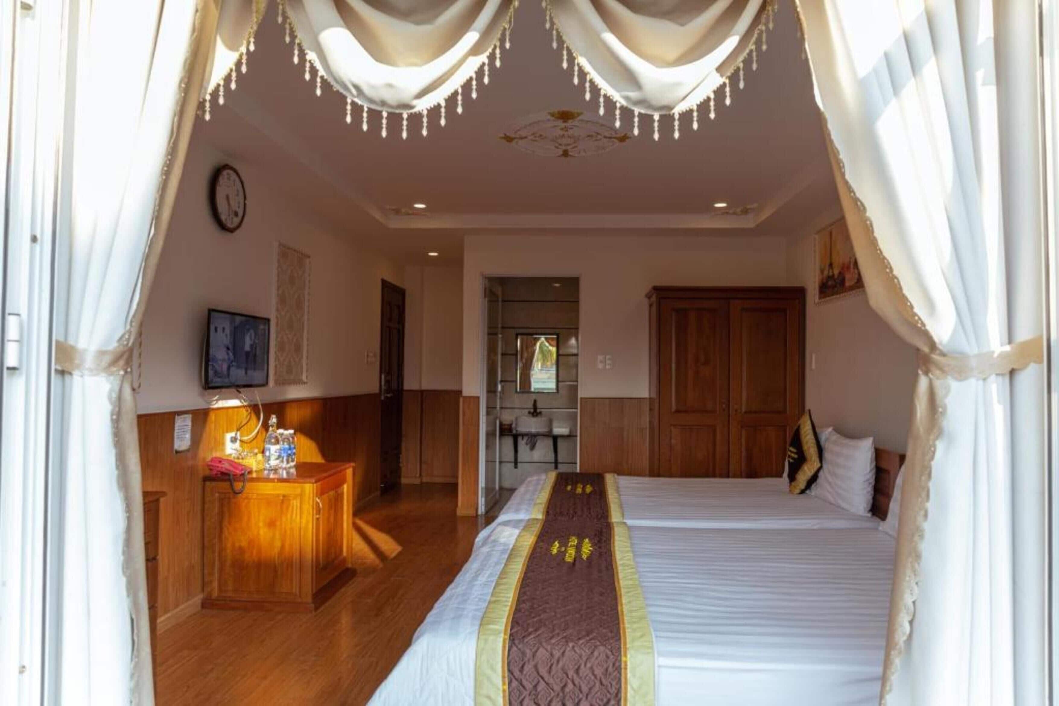 Quarto de hotel com cama, escrivaninha com luminária, espelho e guarda-roupa de madeira.