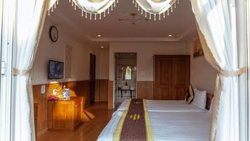 A hotel room with a bed, a desk with a lamp, a mirror, and a wooden wardrobe.