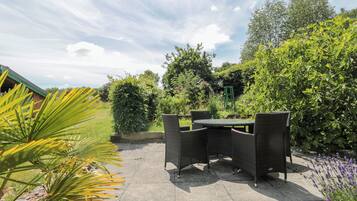 An outdoor patio area with wicker furniture, a concrete floor, and surrounding greenery.