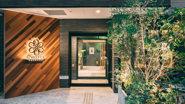 A hotel entrance with a wooden facade, a glass door, and a small outdoor garden area. - R Hotel Honmachi (Osaka)