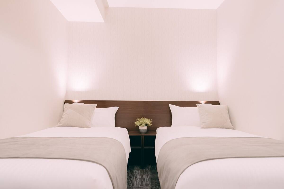 Habitación de hotel con dos camas, una mesita de noche con una planta y un cabecero de madera.