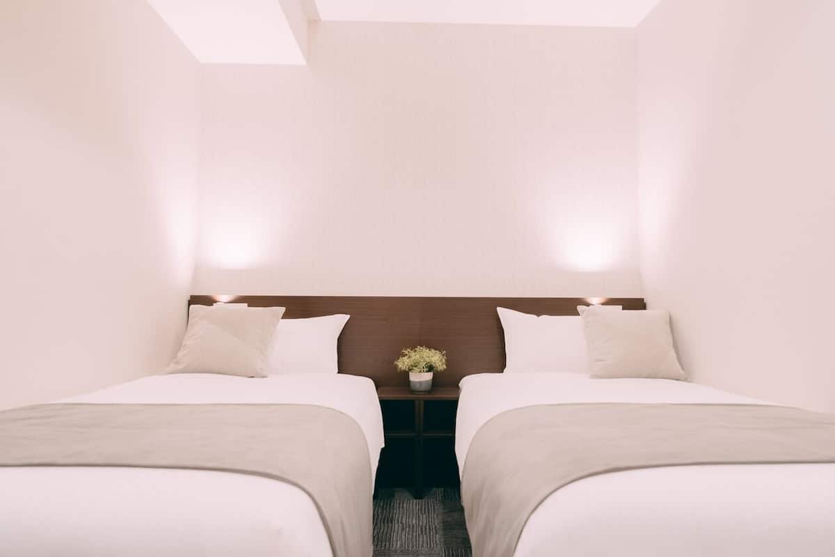 A hotel room with two beds, a nightstand with a plant, and a wooden headboard.