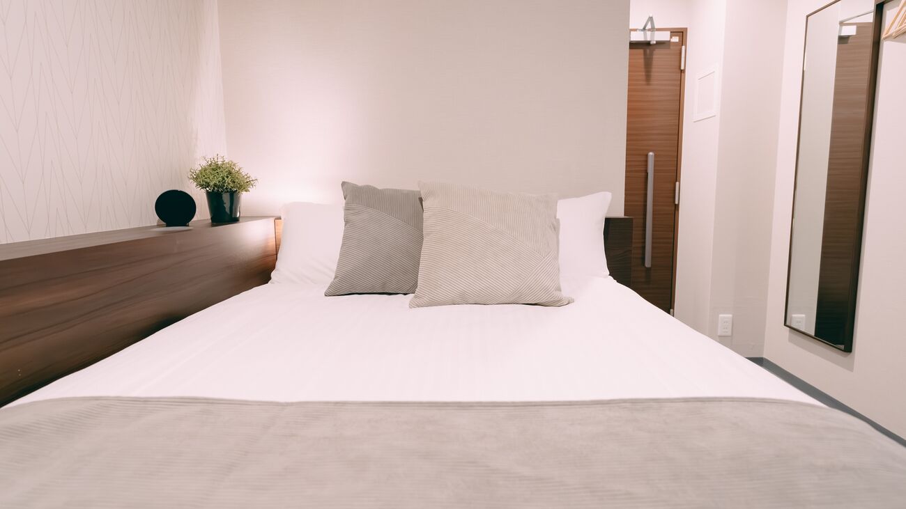 Una cama bien hecha con dos almohadas, una mesita de noche con una planta en maceta y un cabecero de madera.