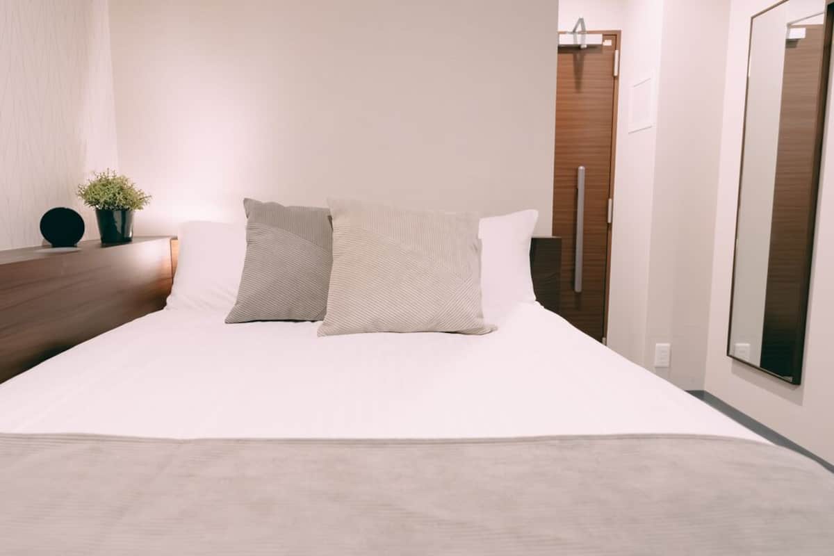 Una cama bien hecha con dos almohadas, una mesita de noche con una planta en maceta y un cabecero de madera.