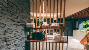 A modern interior with a stone wall, a wooden partition with towels and toiletries, and a potted plant. - R Hotel Honmachi (Osaka)