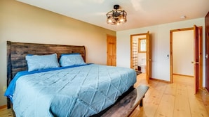 Un dormitorio con cabecera de madera, cama con colcha azul, un banco y una lámpara en el techo.