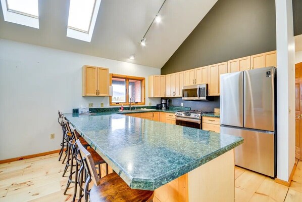 A modern kitchen with a large island, wooden bar stools, and a stainless steel refrigerator. - Cody retreat with a view and hot tub (Cody)