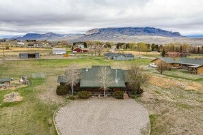A rural property with a large house, a gravel driveway, and a mountainous backdrop. - Cody retreat with a view and hot tub (Cody)