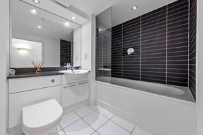 A modern bathroom with a white toilet, a sink, and a bathtub with black tiles.