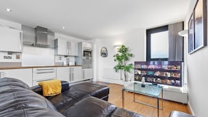 A modern living room with a leather sofa, a glass coffee table, and a flat-screen TV mounted on the wall. - Lovely & Cosy 2 Beds London Skyline View (London)