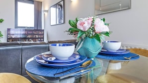 A dining table with blue placemats, white bowls, and a teal vase with flowers. - Lovely & Cosy 2 Beds London Skyline View (London)