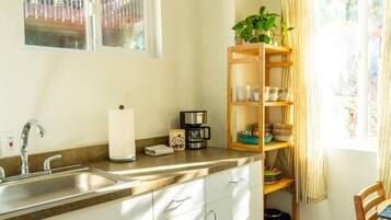 Una cucina con lavello in acciaio inossidabile, una macchina per il caffè e una mensola in legno con stoviglie.