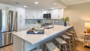 A modern kitchen with white cabinets, stainless steel appliances, a granite countertop, and a central island with bar stools. - Step out to Pool and Beach, Huge Patio, 2nd Pool Heated, Minutes to Downtown, $300 in Free Tickets! (St. Augustine Beach)