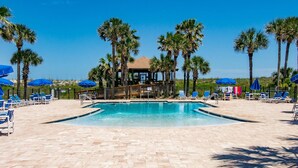 A pool area with lounge chairs and umbrellas, surrounded by palm trees. - Step out to Pool and Beach, Huge Patio, 2nd Pool Heated, Minutes to Downtown, $300 in Free Tickets! (St. Augustine Beach)