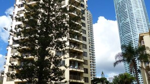 A high-rise building with multiple balconies and a modern glass facade, adjacent to a shorter building with a flat roof and a sign for 'Aloha'. - One Bed Room Ocean View With Surfers Holiday Accommodation - Aloha Apartments (Surfers Paradise)