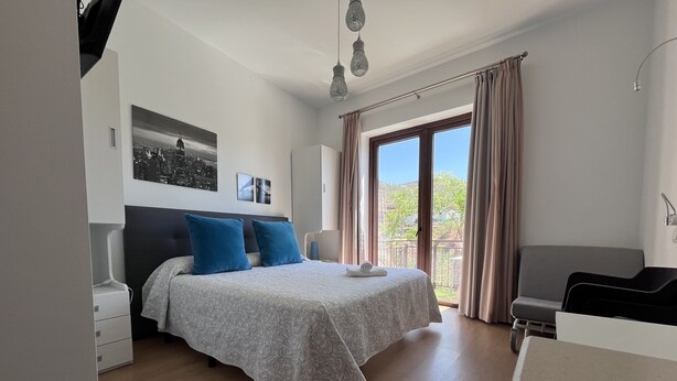 Une chambre à coucher avec un lit, un bureau et un balcon agrémenté de rideaux.