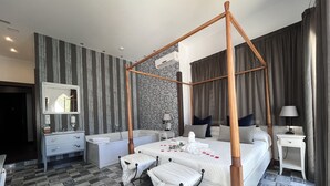 Une chambre moderne avec un lit à baldaquin, un coin salon avec un banc, une coiffeuse avec un miroir et une salle de bain avec une baignoire.