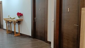 Un couloir avec deux portes en bois, l’une portant le numéro « 1 » et l’autre le numéro « 2 », et une petite table ornée d’objets décoratifs.