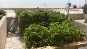 Un espace aménagé avec un chemin pavé, une grille en métal et une vue sur la plage, où l'on aperçoit des personnes au loin.