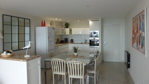 Une cuisine moderne avec des meubles blancs, un réfrigérateur, une machine à café et une table à manger avec des chaises.