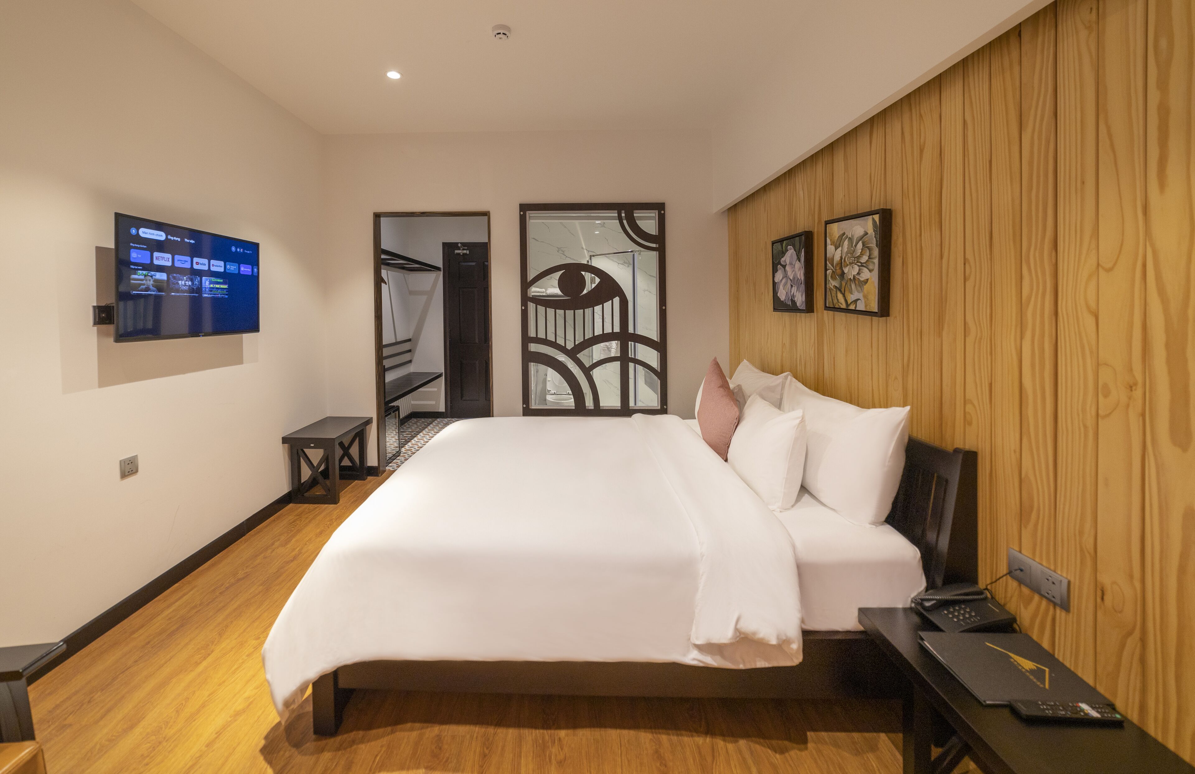 Una habitación de hotel moderna con una cama grande, un televisor de pantalla plana en la pared, un panel de pared de madera y una mesita con un control remoto.