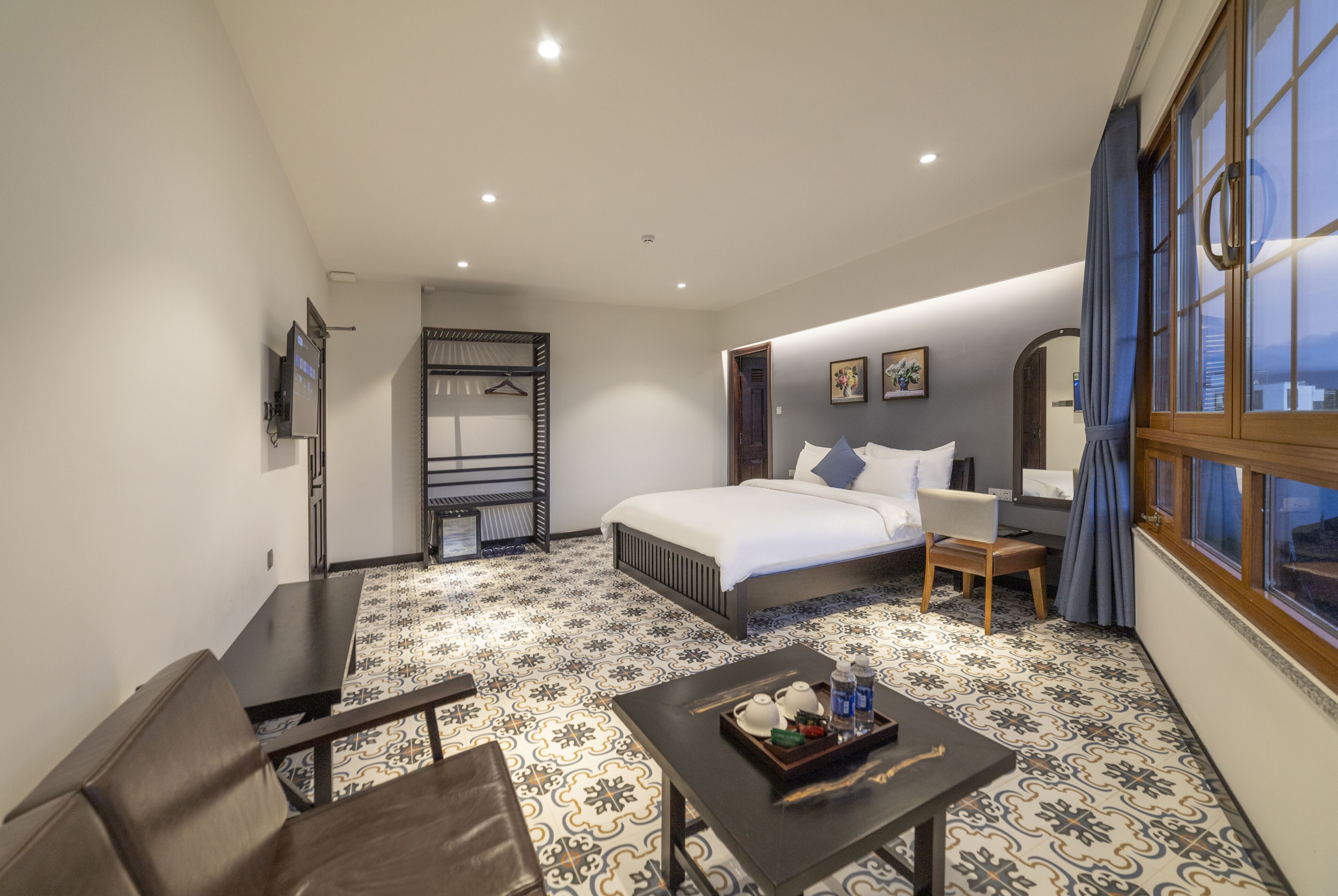 Habitación de hotel con cama, escritorio, silla, una mesita con una bandeja de objetos y ventana con cortinas.