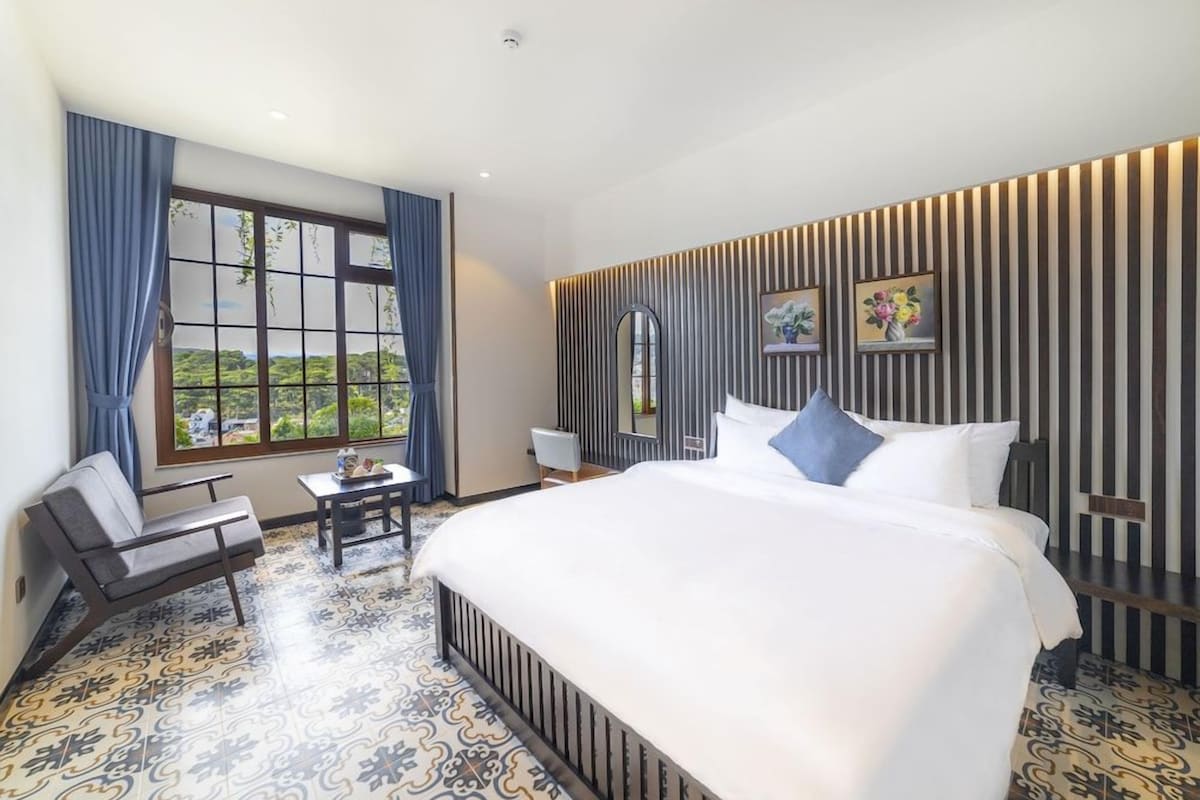 Habitación de hotel con una cama grande, un escritorio, una silla y vistas a zonas verdes por la ventana.