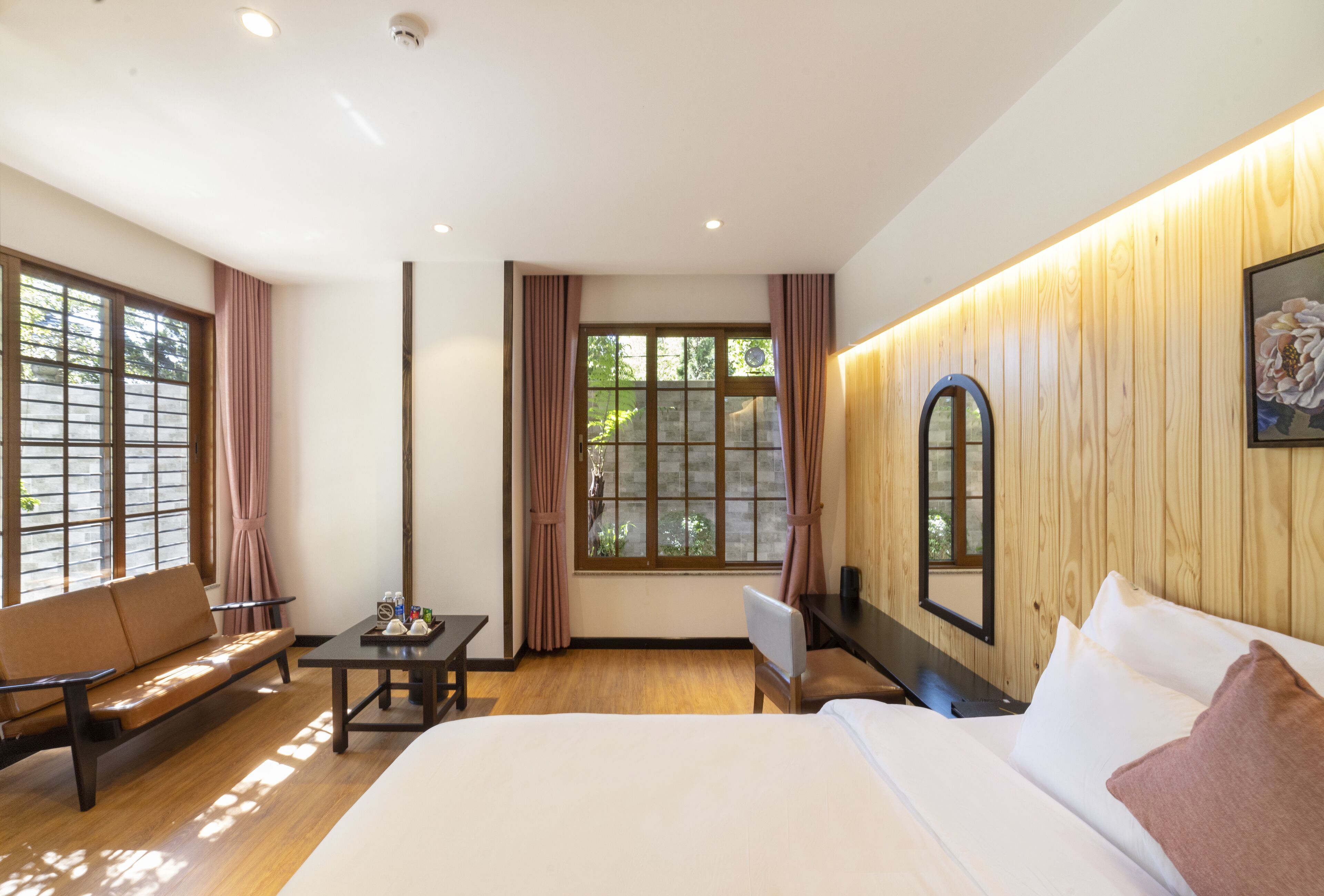 A hotel room with a bed, a sofa, a desk, and a window with curtains.