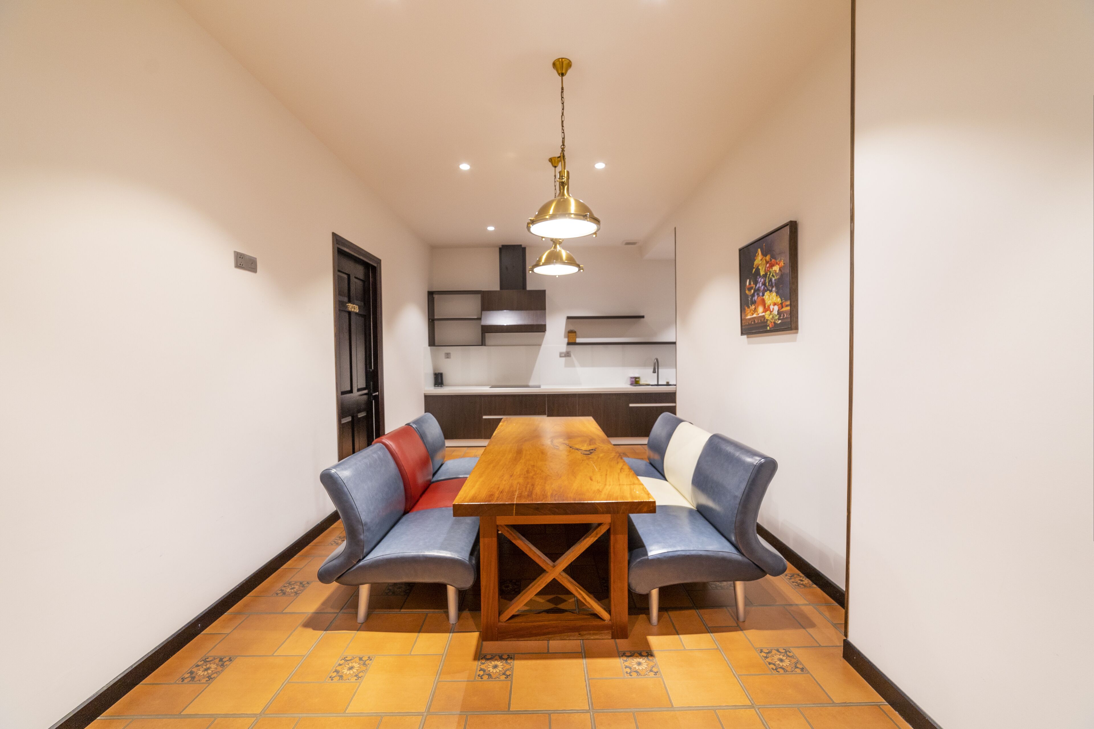 Un coin repas avec une table en bois et des chaises à revêtement bleu, une cuisine en arrière-plan et un luminaire suspendu au-dessus.