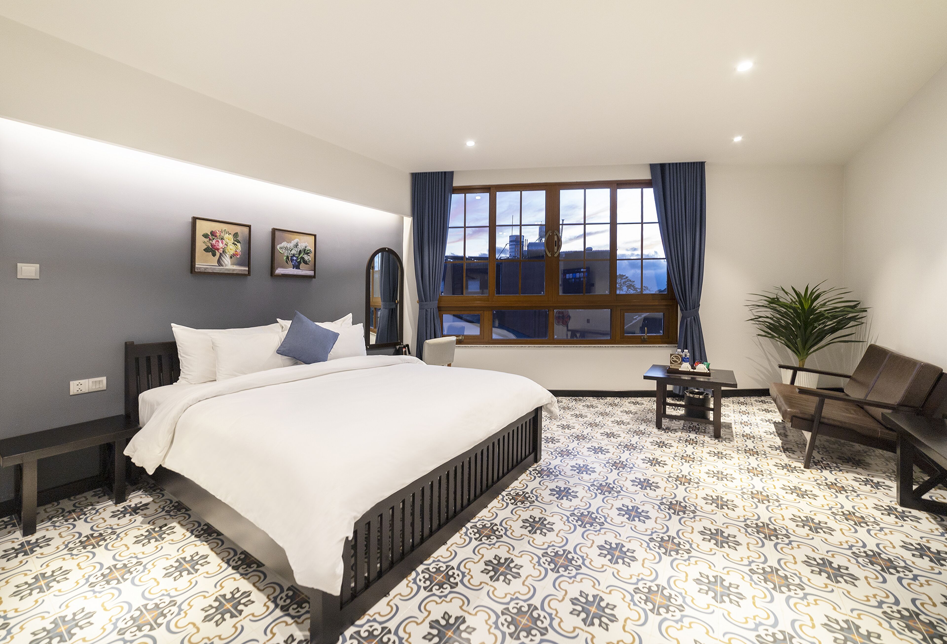 A bedroom with a large bed, a desk, a chair, and a window with curtains.