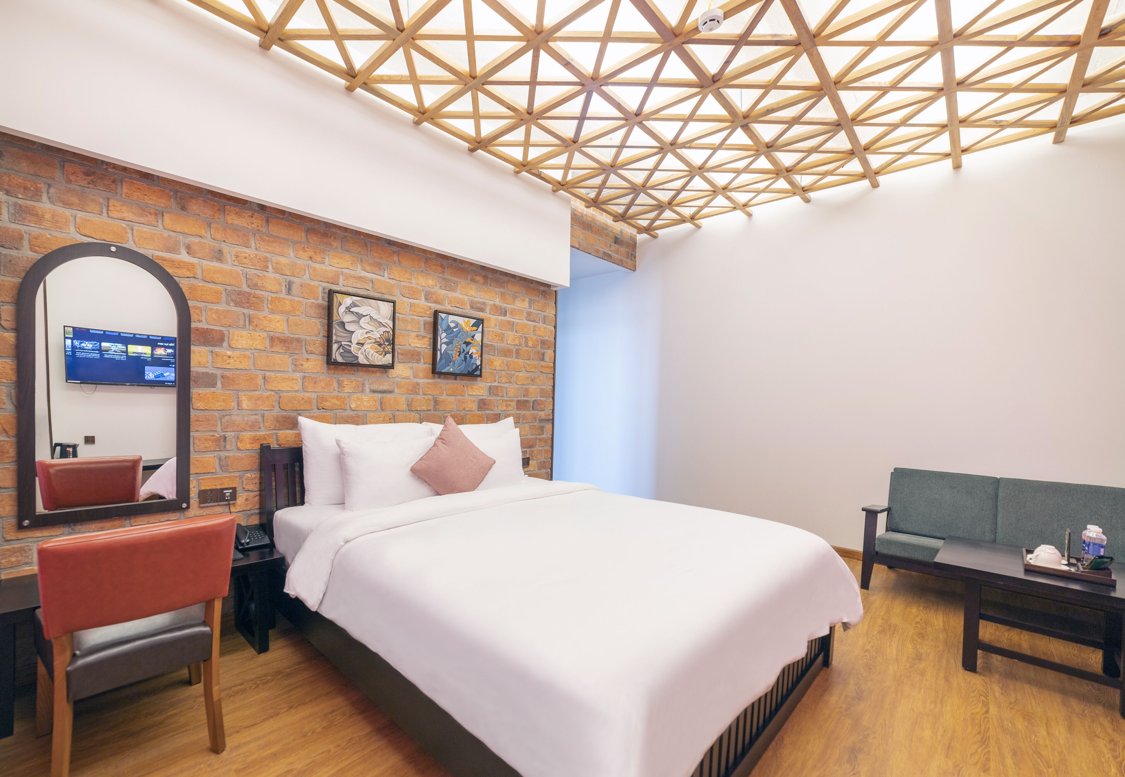 Een moderne hotelkamer met een bakstenen muur, een houten plafond, een bed met witte beddengoed, een bureau met stoel en een groene bank.