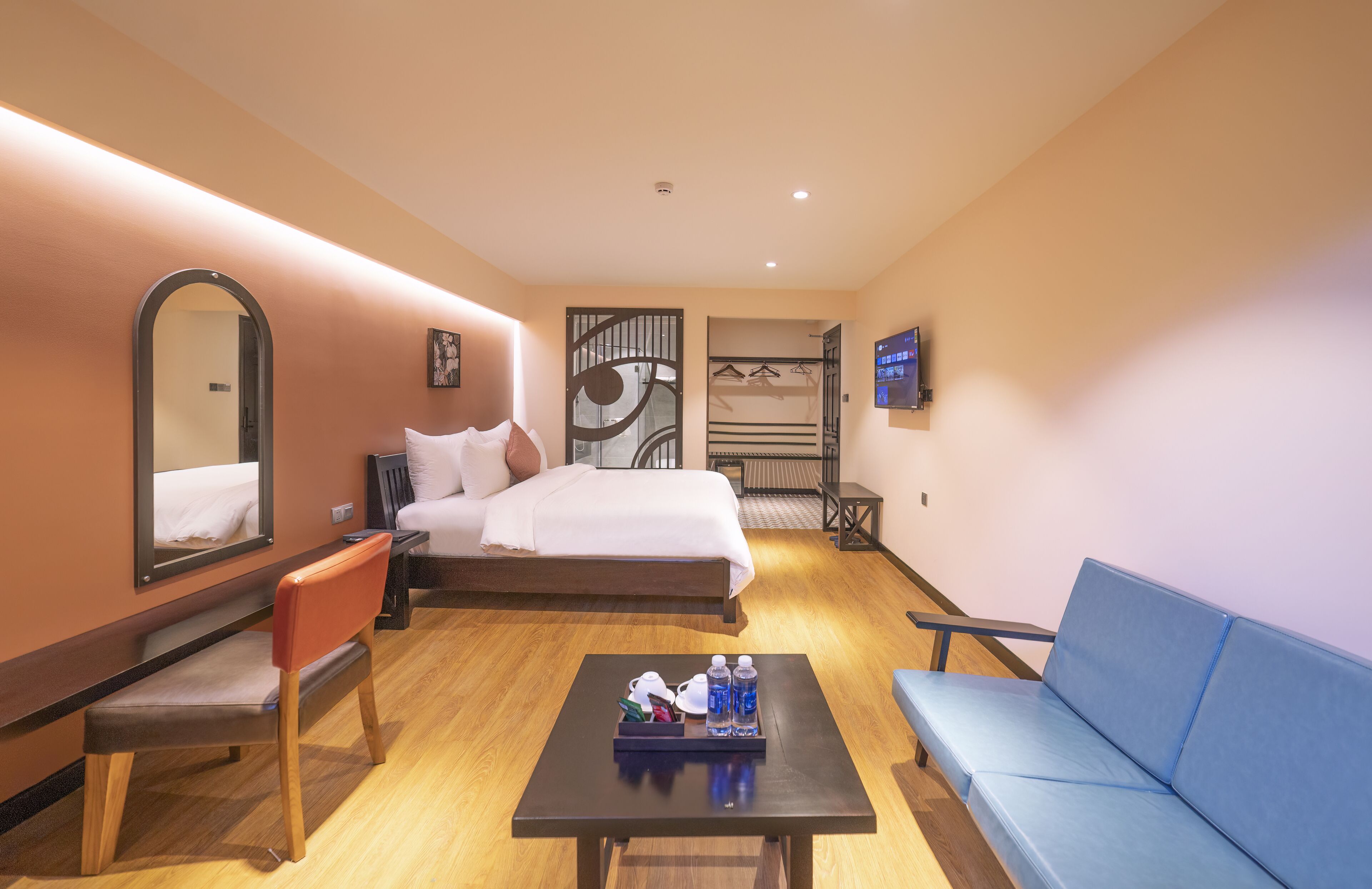 A hotel room with a bed, a desk with a tray of toiletries, a blue sofa, a chair, a TV, and a mirror.