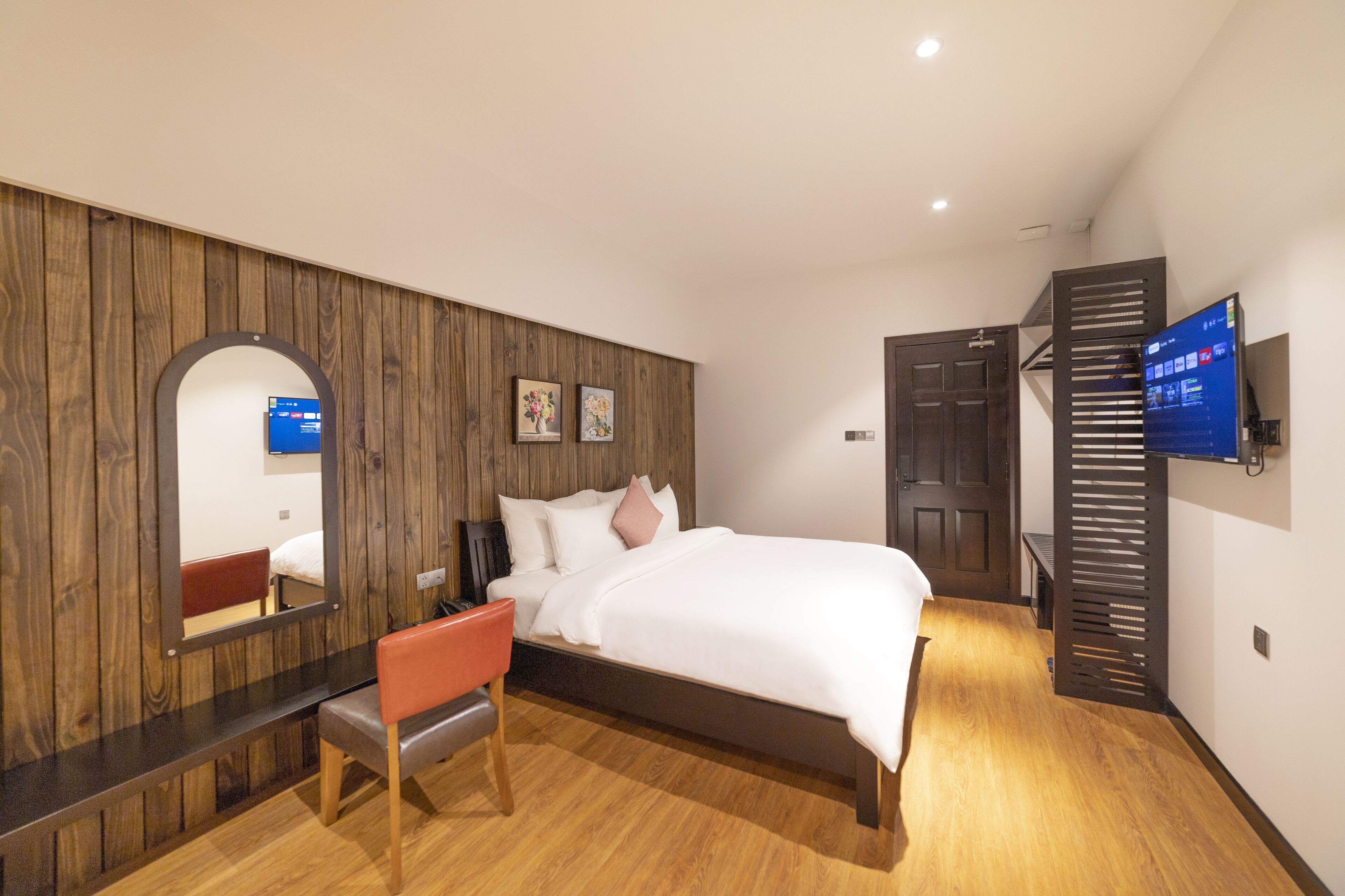 A modern hotel room with a wooden accent wall, a large bed, a desk, and a TV mounted on the wall.
