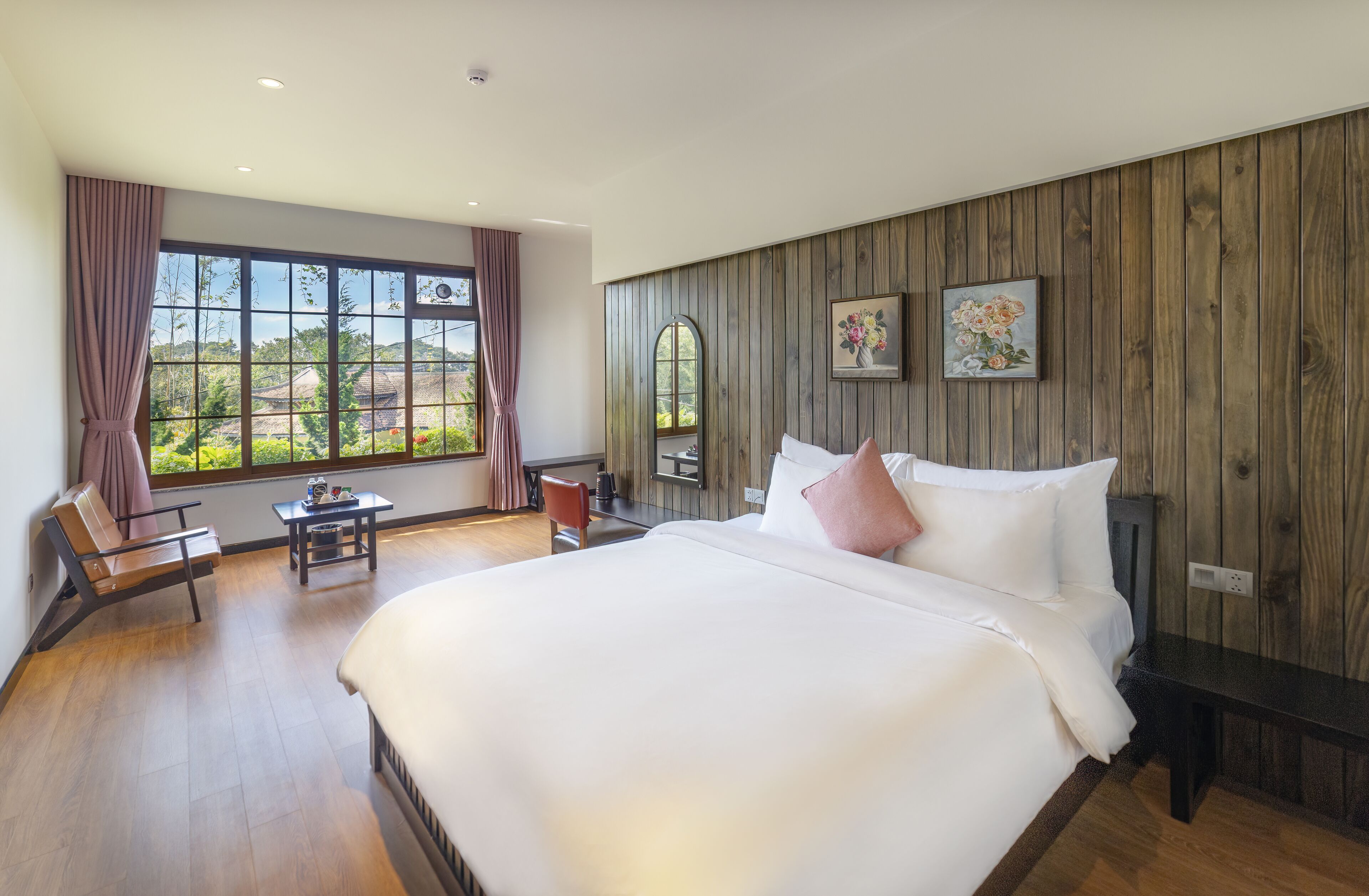 Un dormitorio espacioso con una cama grande, paneles de madera, una ventana con cortinas, una pequeña mesa y un banco.