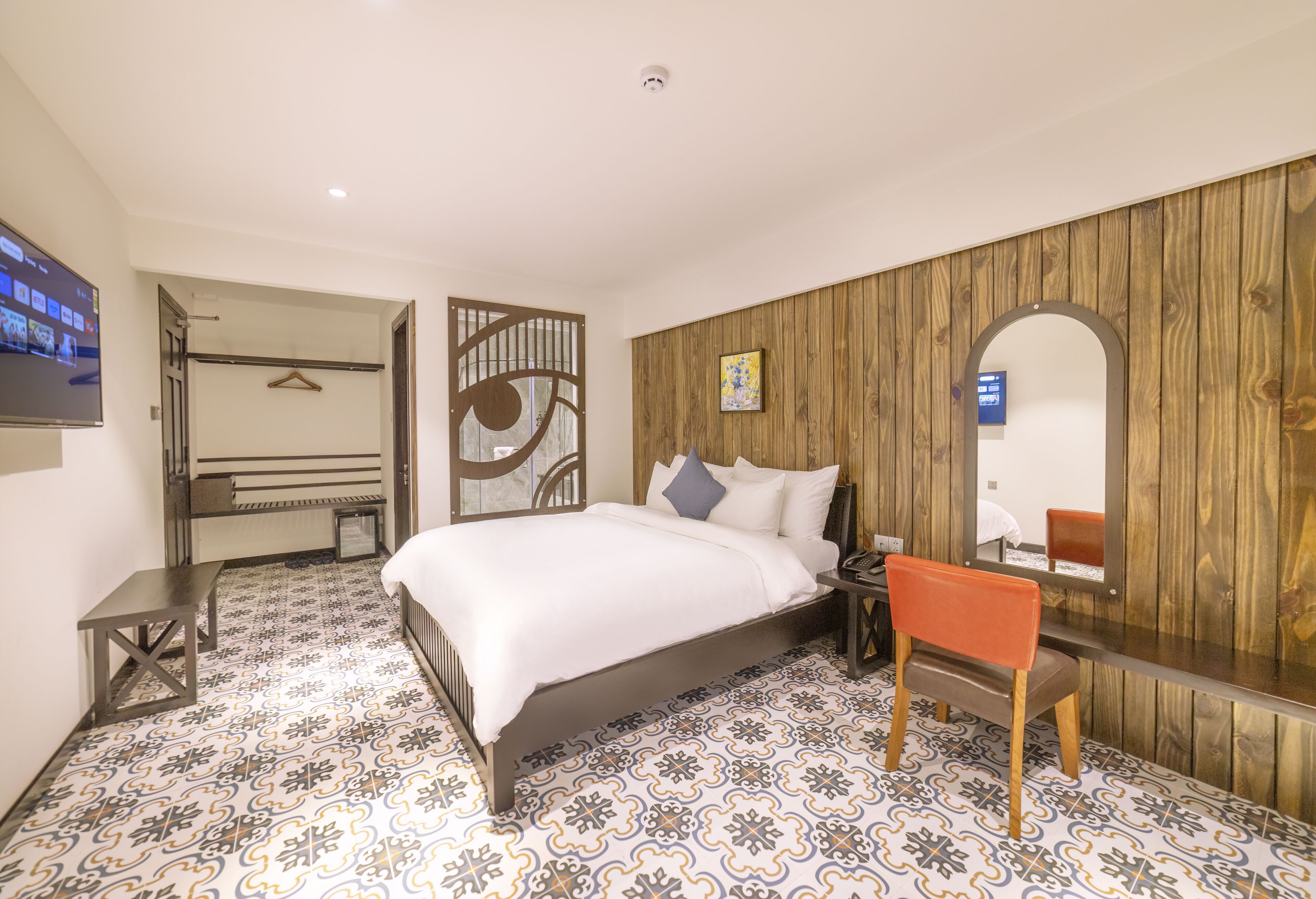 A bedroom with a bed, a wooden panel wall, a mirror, and a tiled floor.