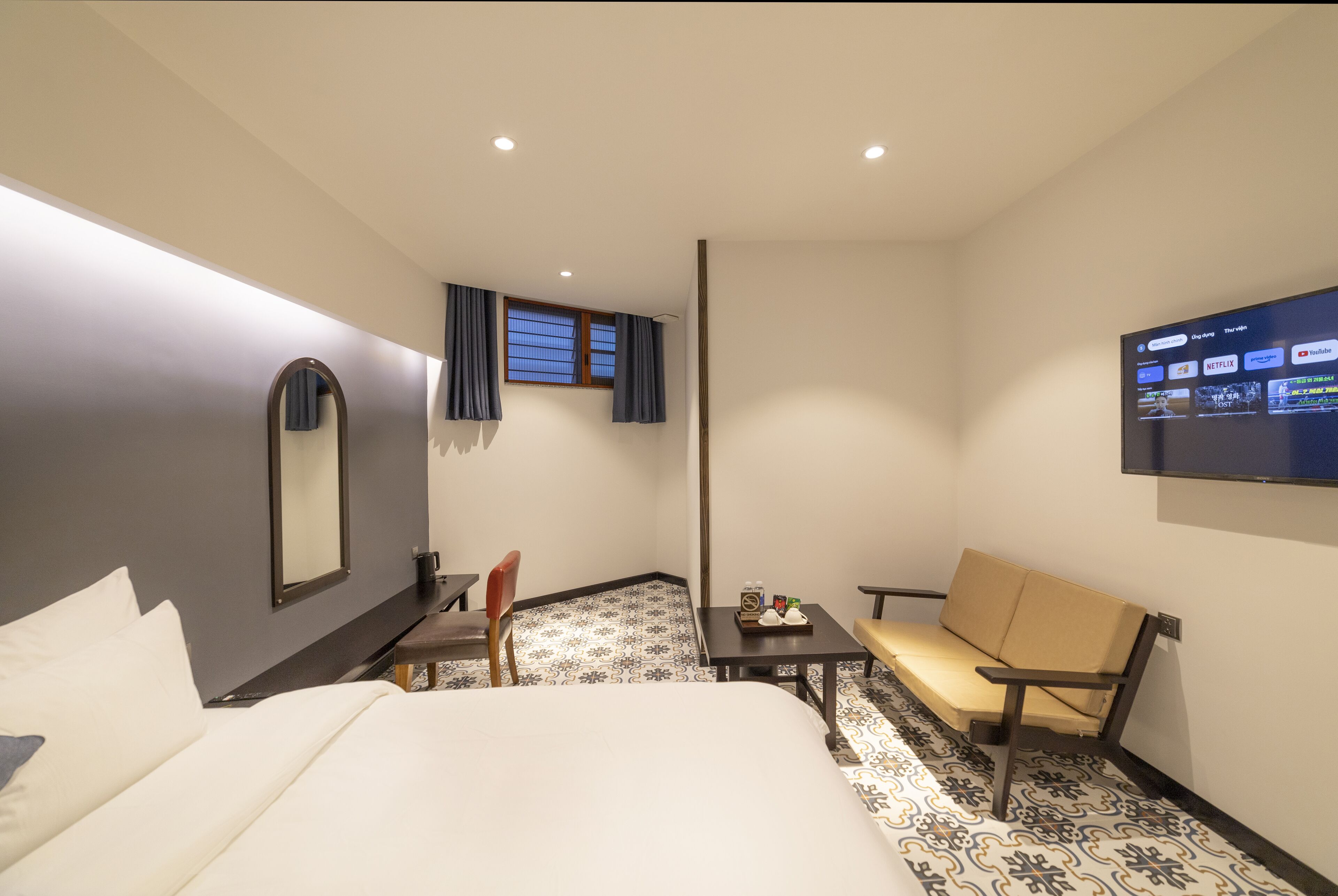 Habitación de hotel con cama, escritorio, silla, sofá, televisor montado en la pared y ventana con cortinas.