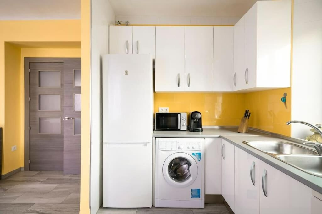 A compact kitchen with white cabinets, a washing machine, a microwave, and a sink.
