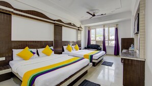 A hotel room with two beds, a ceiling fan, a window with curtains, and a small table with a bottle. - Itsy Hotels Satya Shree (Reasi)