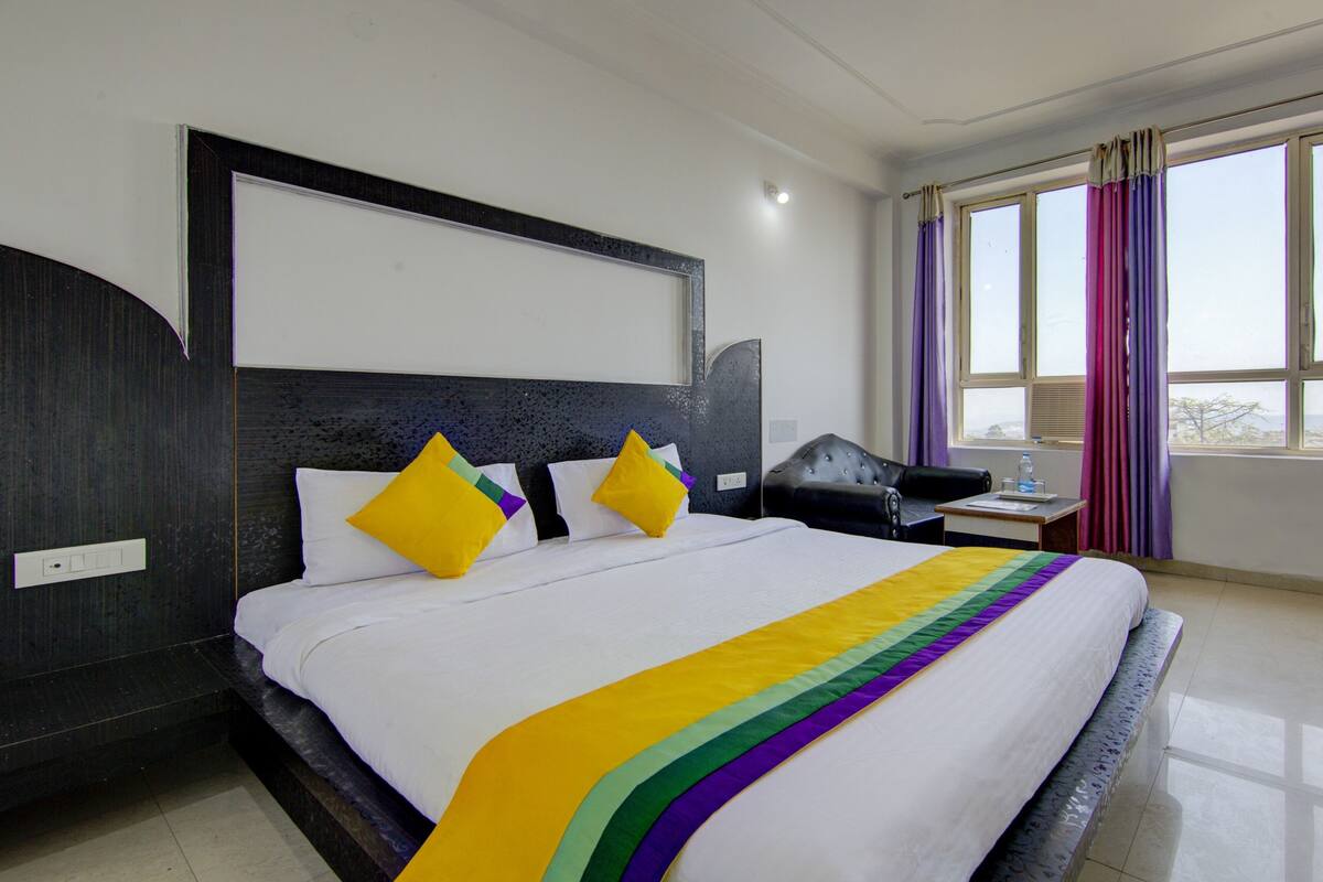 Habitación de hotel con una cama grande, cabecera, escritorio y ventana con cortinas.