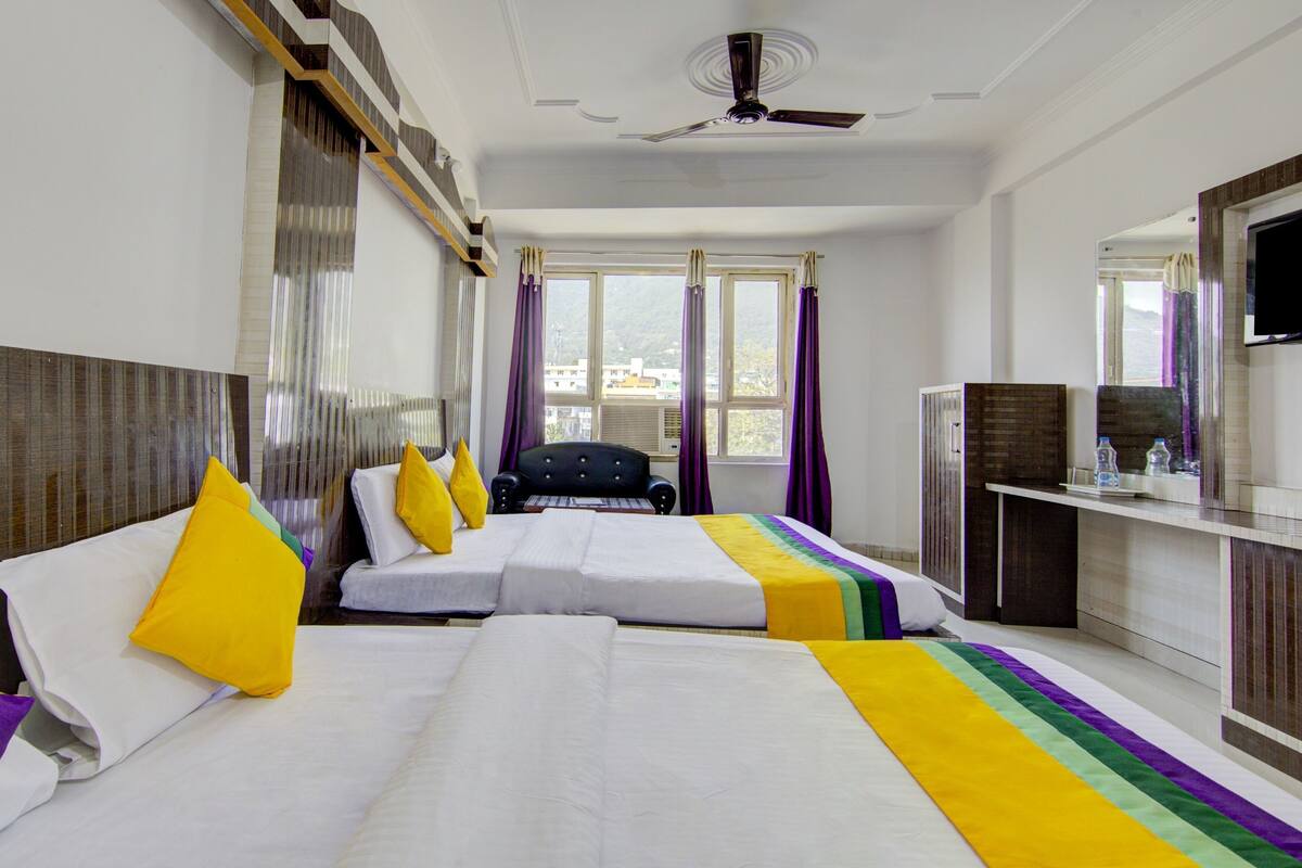 Habitación de hotel con dos camas, televisión, escritorio y ventana con cortinas.