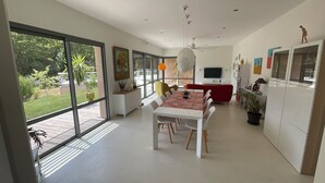 A modern kitchen with white cabinets, a dining area with a white table and chairs, and a red sofa.