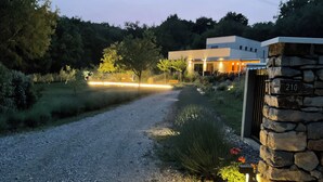 A gravel driveway leading to a modern house with a stone wall and the number 210.