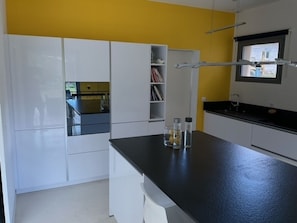 A modern kitchen with white cabinets, a black countertop, and a yellow accent wall.